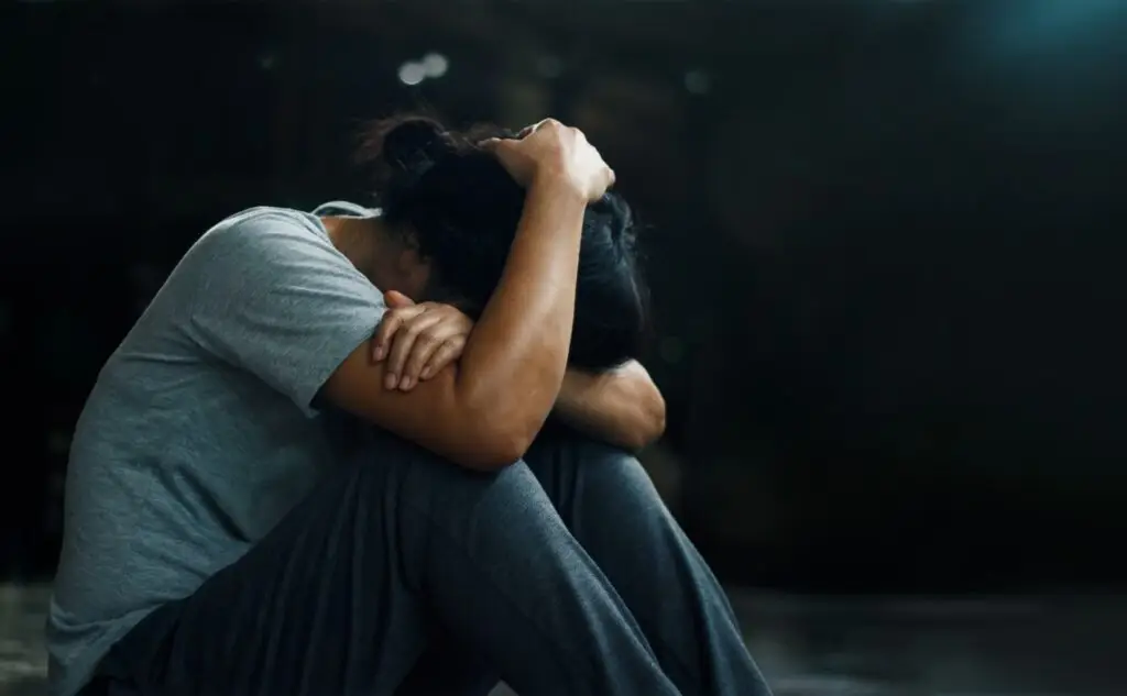 Person sitting curled on the floor with head in their arms, conveying distress or sadness.